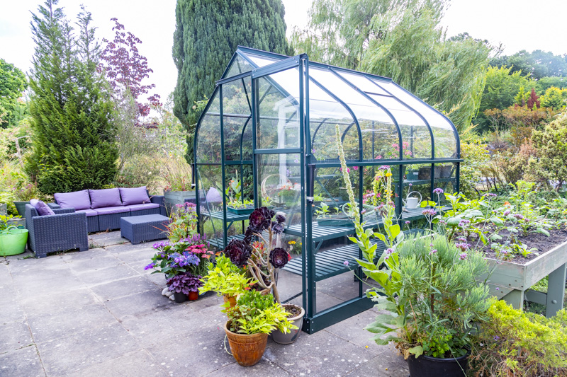 Greenhouse on stone slab patio surrounded by various potted plants